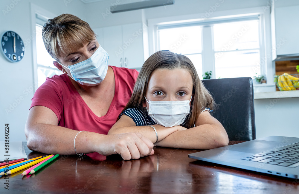 Coronavirus school closures and lockdown. Mum and bored daughter with masks studying online at home