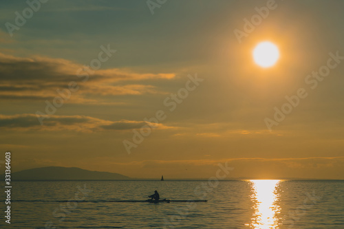 Kayaker or a person in a paddle boat on a lake during evening hours. Romantic leisure activity on the water. Sun about to set into the water.