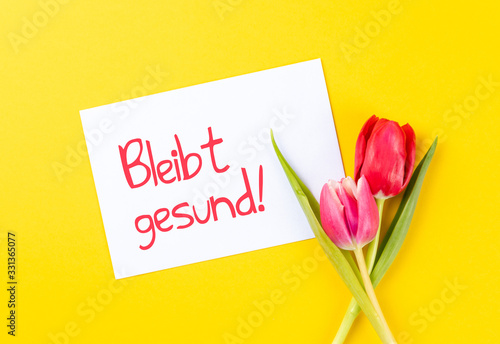 colorful tulips and yellow background with german text bleibt gesund, in english stay healthy