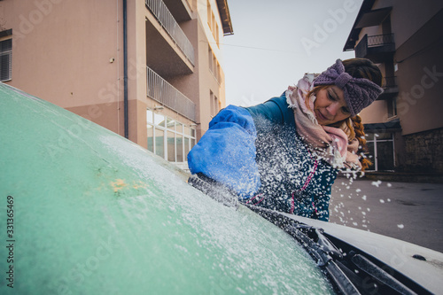 Foto Woman is cleaning an icy window on a car with ice scraper