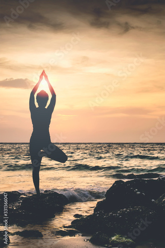 Silhouette of woman doing yoga with seascape and sunset backgound. © NAMPIX
