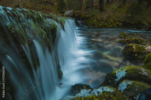 Small water dam at the river spring of Kamniska Bistrica in Slovenia in dry winter time. Cold enchanted waterfall with flowing water in the middle of the forest.