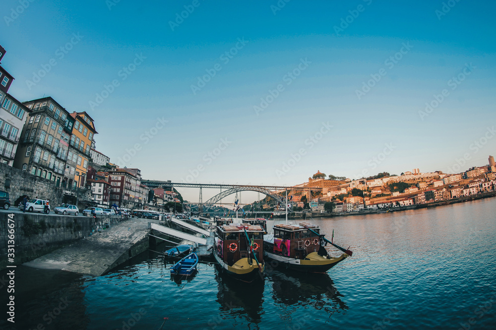Water view of the bridge in Porto on a late afternoon with boats in the foreground.