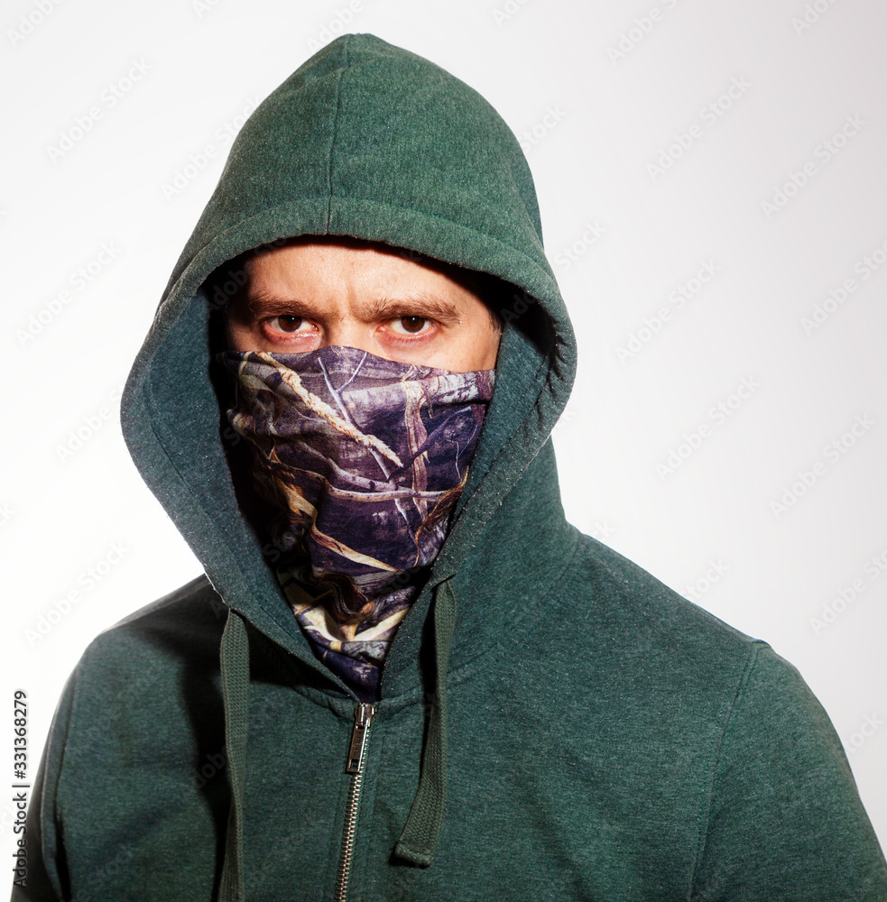 A man wearing a mask and a hood looks into the camera. Close up