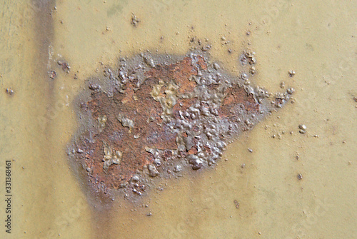 A stain of brown rust on a khaki-colored metal surface. Bubble-blown corrosion.