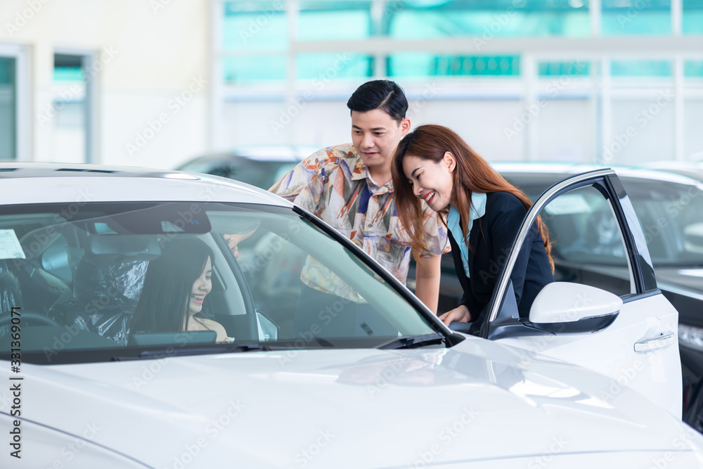 Beautiful young couple choosing a car at the dealership talking to the salon manager in a new car at the dealership professional salesman showing the automobile characteristics buying cars. Beautiful young couple choosing a car at the dealership talking to the salon manager in a new car at the dealership professional salesman showing the automobile characteristics buying cars.