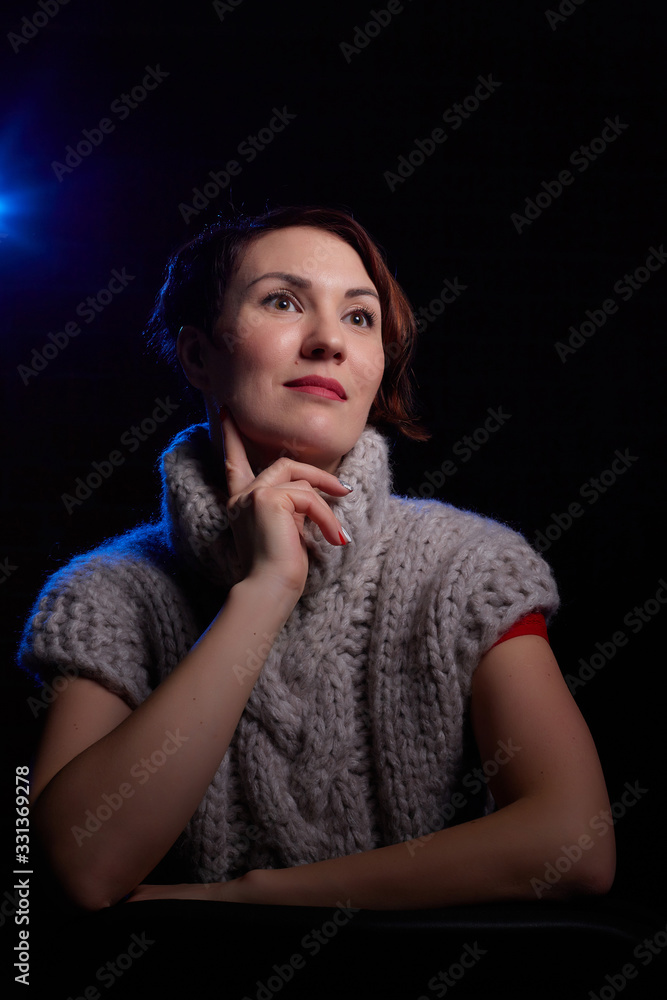 Portrait of a beautiful, charming young woman in in a grey thick knitted sweater and a black background. Model posing doring studio photo shot Portrait of a beautiful, charming young woman in in a grey thick knitted sweater and a black background. Model posing doring studio photo shot