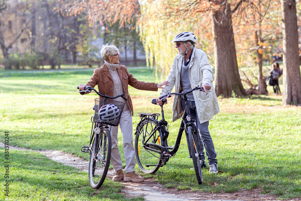 Senior couple with bycicles and helmets in park Senior couple with bycicles and helmets in park