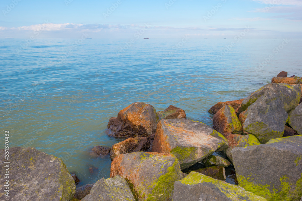 Dike along a lake in sunlight below a blue cloudy sky in winter Dike along a lake in sunlight below a blue cloudy sky in winter