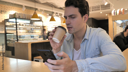 Young Man Using Smartphone and Drinking Coffee in Cafe