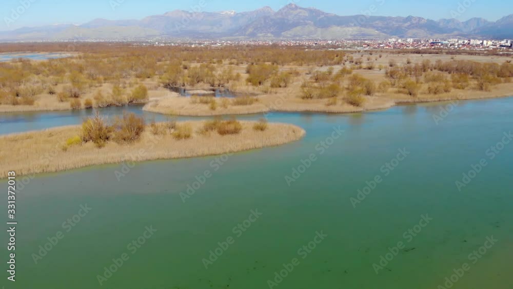 Calm lagoon on shore of Scutari lake, dry brown reeds countryside and mountains background on a sunny day Calm lagoon on shore of Scutari lake, dry brown reeds countryside and mountains background on a sunny day