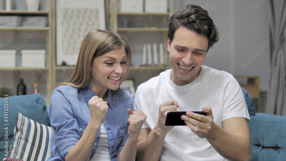 Cheering Young Couple Excited for Success while Watching on Smartphone Cheering Young Couple Excited for Success while Watching on Smartphone