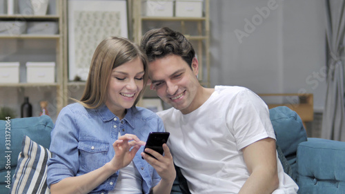 Happy Young Couple Browsing Internet on Smartphone at Home