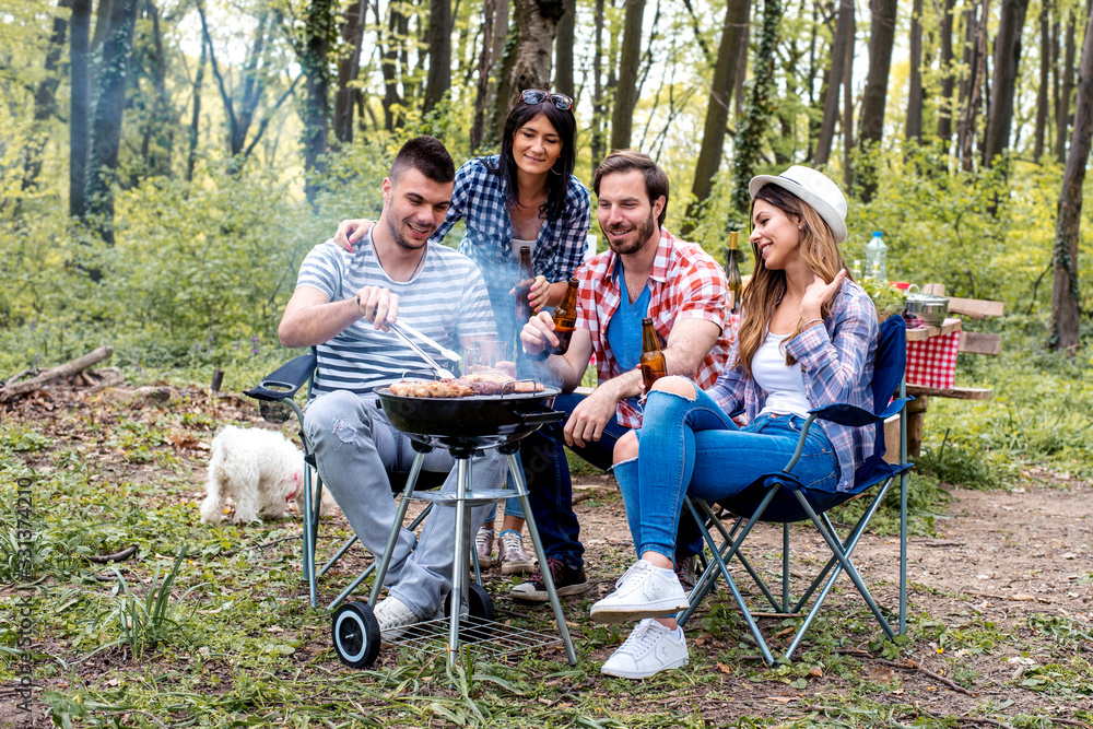 Group of friends having a barbecue party in nature and enjoying picnic day together