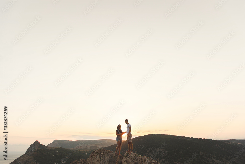 Lovers, guy and girl, on the edge of the cliff against the backdrop of mountains and ocean.