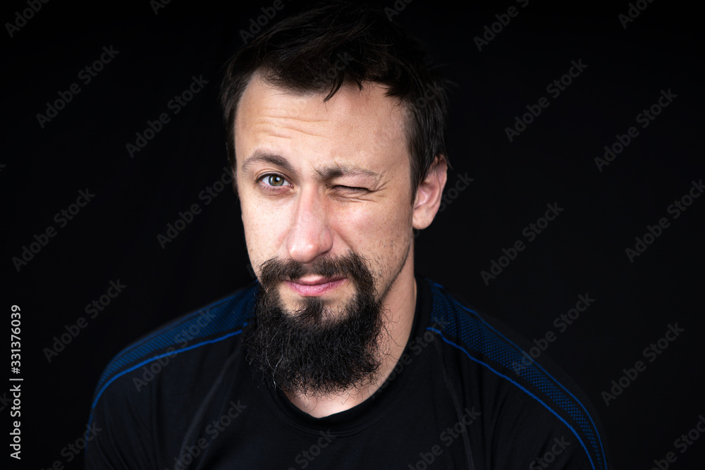 a close up portrait of a young man with beard in dark clothes on a dark background