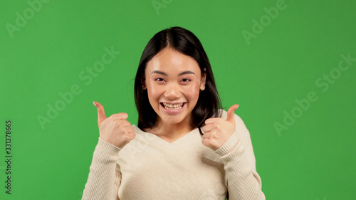 Asian model showing thumbs up and smiles. Excited beautiful woman on isolated background.