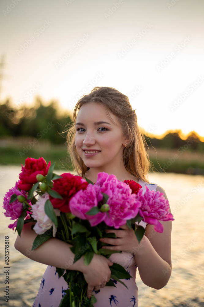 vertical portrait of a smiling young girl with a bouquet of blossoming peonies on the background of the river vertical portrait of a smiling young girl with a bouquet of blossoming peonies on the background of the river