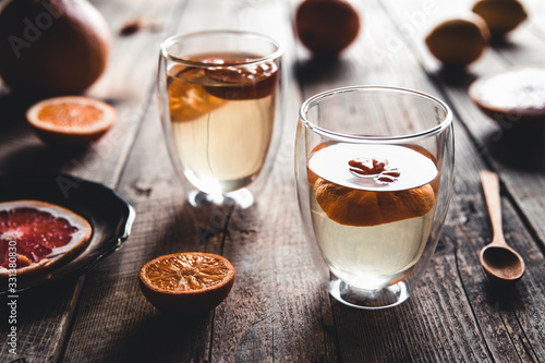 Citrus tea in a transparent teapot and a glass, healthy drink on a wooden background.