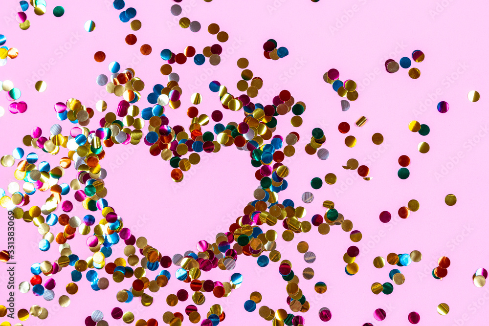 Heart shape made of golden colorful confetti splash on pink background. Festive backdrop of sparkles for birthday, valentine's day, carnival Heart shape made of golden colorful confetti splash on pink background. Festive backdrop of sparkles for birthday, valentine's day, carnival