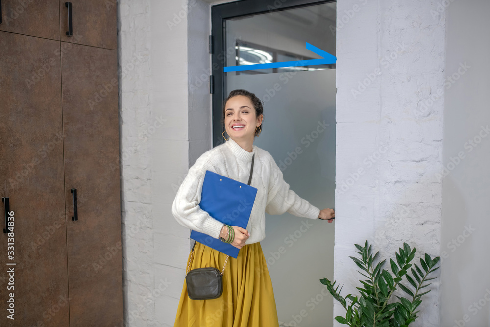 Young woman standing at the door, holding door hangle, smiling
