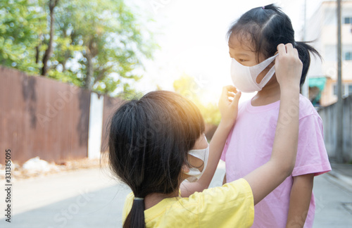 Young Asian girl wearing mask for sister to protect covid 19, Thai kid wear dust mask. Protect pm 2.5 and stop  corona virus concept