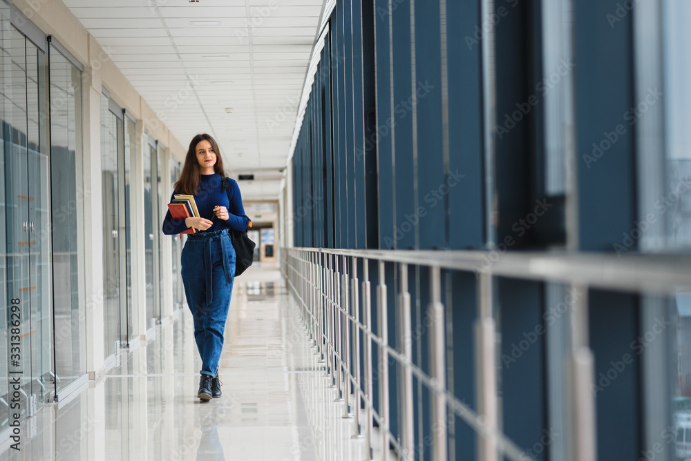 Portrait of a pretty female student with books and a backpack in the university hallway