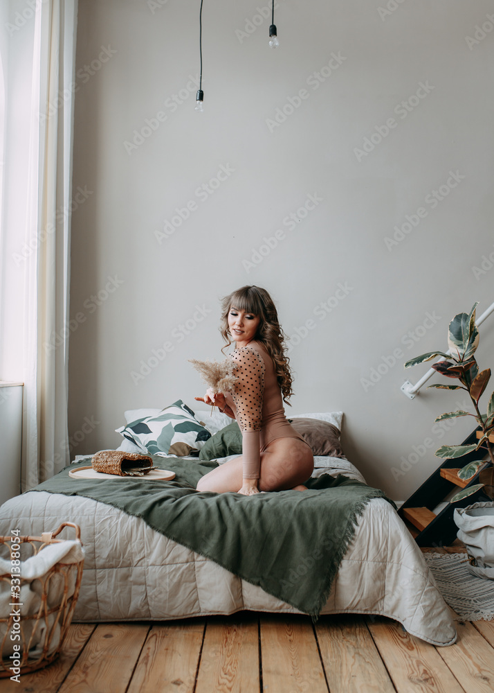 Attractive happy seductive sensual beautiful girl a woman in a bodysuit is awake and lying on the bed in her bedroom, resting and relaxing, a joyful girl meets the morning in a bright room