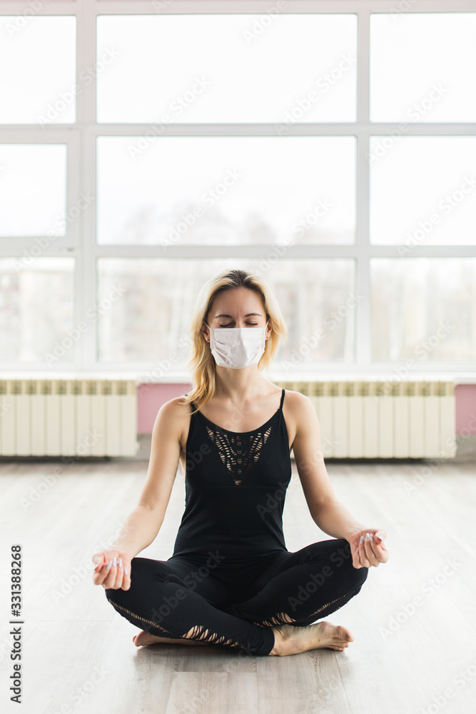 A girl in a medical mask does yoga in a closed Studio in sports clothes. Quiet meditation in the face of a virus epidemic. A girl in a medical mask does yoga in a closed Studio in sports clothes. Quiet meditation in the face of a virus epidemic.
