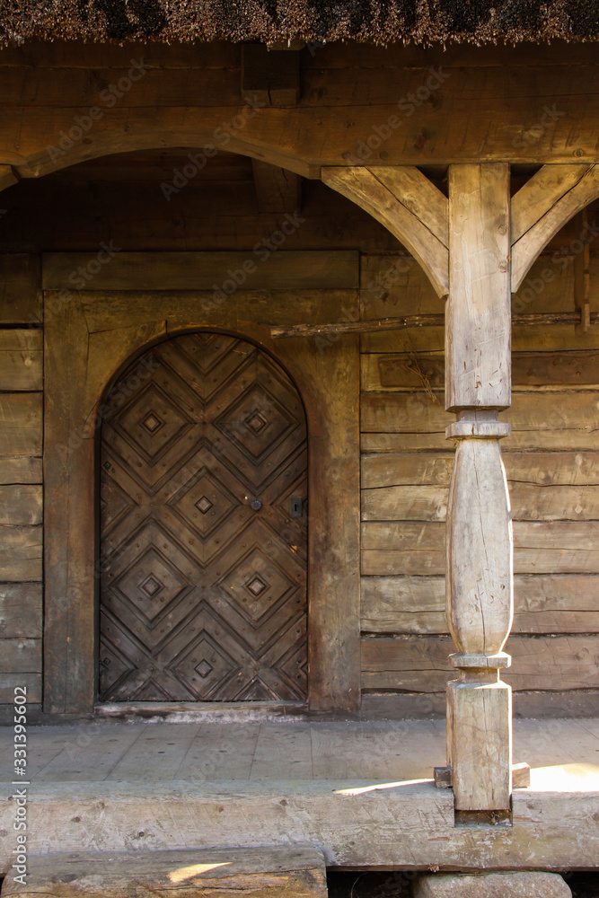 A threshold in front of the wooden log house with a carved door. Arch and a carved pillar at the terrace.