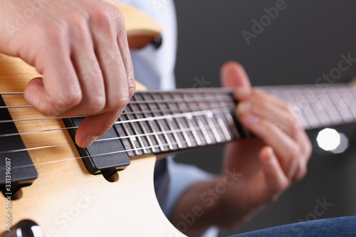 Fototapeta Male arms holding and playing classic shape wooden electric guitar closeup. Six stringed learning musical school education art leisure electrical vintage stage shop having fun enjoying hobby concept