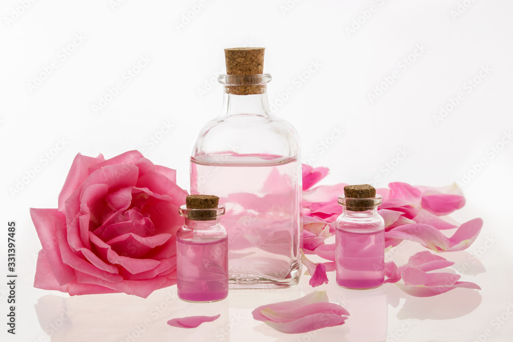 Rose water and oil in glass bottles with flowers on whi Rose water and oil in glass bottles with flowers on whi