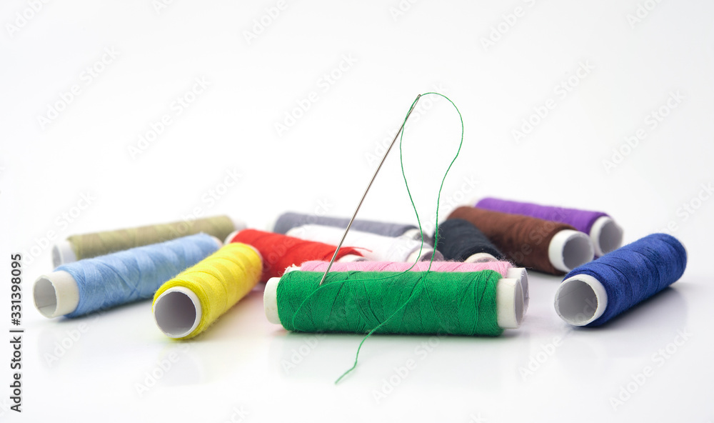 Colorful sewing thread rolls with needle on green roll isolated on white background.Full dept of field. Craft concept. Colorful sewing thread rolls with needle on green roll isolated on white background.Full dept of field. Craft concept.