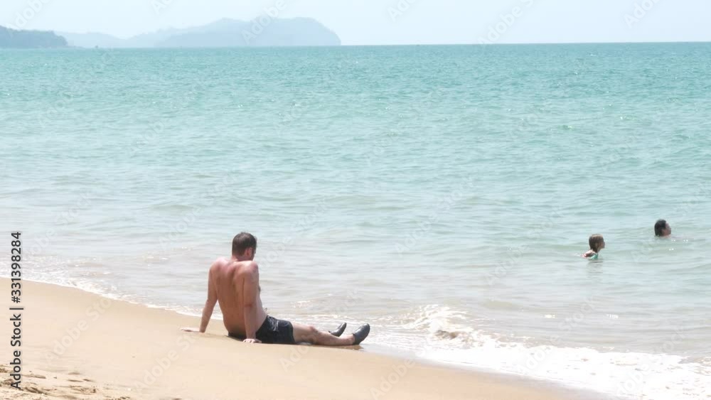 Man lying on beach watching children while playing in sea. Slow motion Man lying on beach watching children while playing in sea. Slow motion