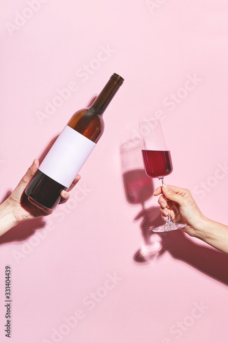Hands holding a glass of wine and a bottle on pink background. Glass of  wine in female hand. Party insta time.