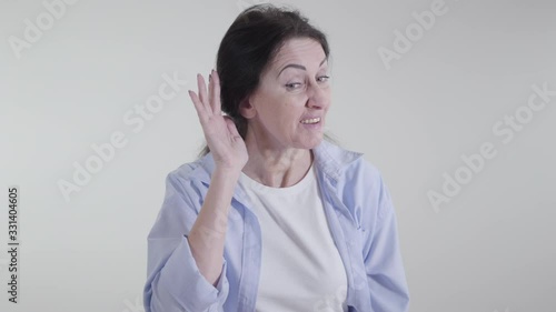 Portrait of brunette woman putting hand to ear and looking at camera with interest. Positive Caucasian lady posing on white background. Concept of gossiping, rumors, hearing. photo