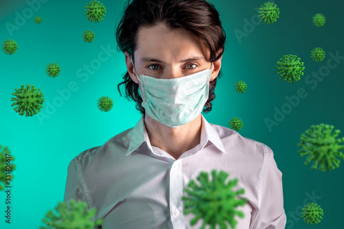 Portrait of a young man in a medical mask surrounded by COVIND-2019 coronavirus on a green background. photo