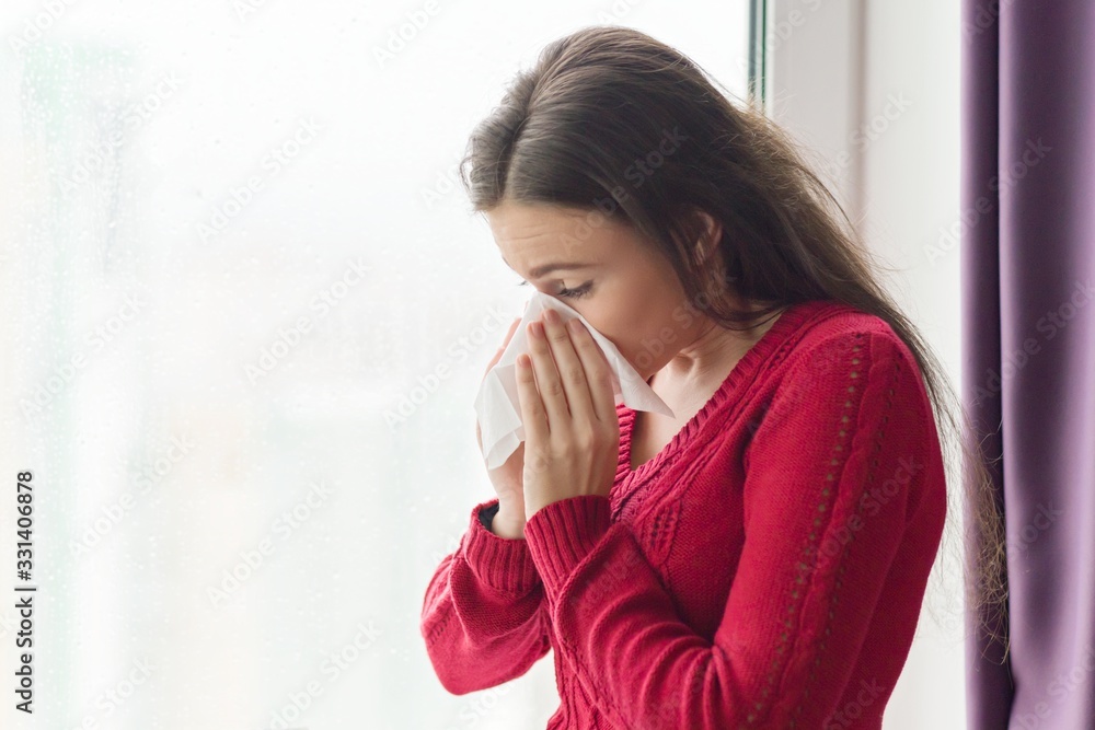 Female with cough, snot, temperature standing at home near window Female with cough, snot, temperature standing at home near window