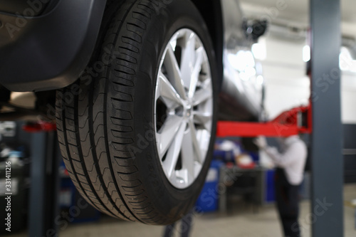 Close-up view of car all-season tire with aluminum rim. Mechanical lift for vehicle. Automobile service center or workshop concept. Professional auto maintenance © H_Ko