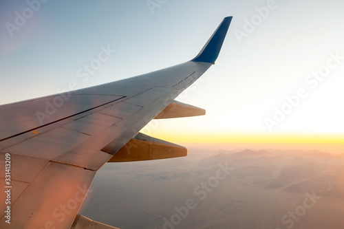 View from airplane on the aircraft white wing flying over desert landscape in sunny morning. Air travel and transportation concept.