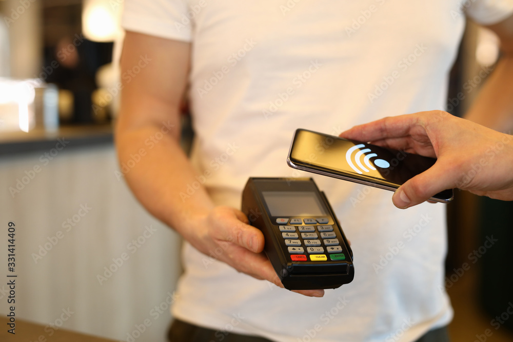 Close-up of customer person making payment via terminal and mobile phone in cafe. Pay by smartphone. Contactless nfc and modern device technology concept Close-up of customer person making payment via terminal and mobile phone in cafe. Pay by smartphone. Contactless nfc and modern device technology concept