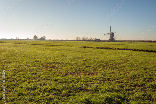 Typical Dutch poilder landscape with windmill. In the background is the historic wooden hollow post mill Scheiwijkse Molen, built in 1638, in the village of Hoornaar, Alblasserwaard, South Holland