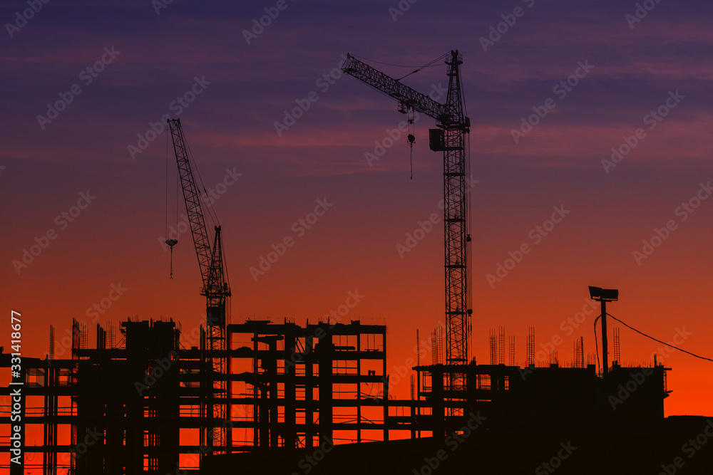 silhouettes of construction cranes at sunset. construction of houses.