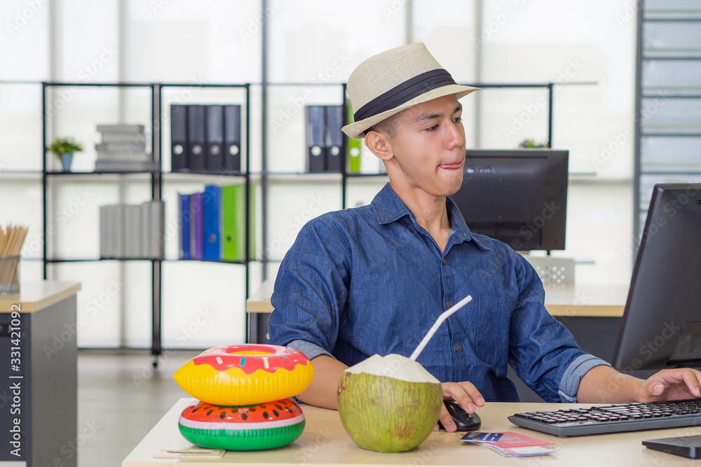 Fototapeta premium Young Asian man wearing a hat and working at the computer while sitting in the office