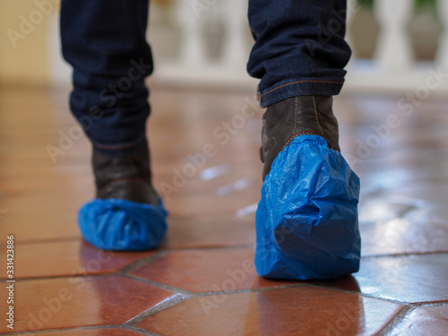 Man with blue shoe covers worn over boots with red shoe laces standing on a tiles, closeup side view.