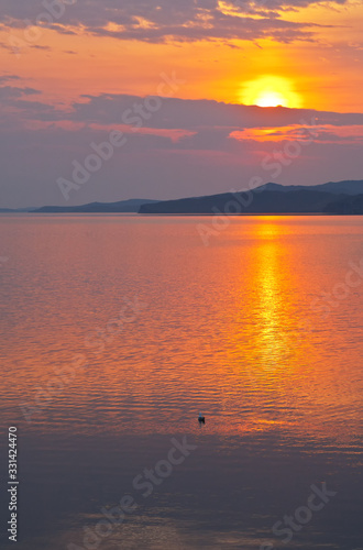 Baikal Lake in spring morning. Beautiful bright sunrise is reflected in the water of the Small Sea Strait. Dawn waterscape. Natural background