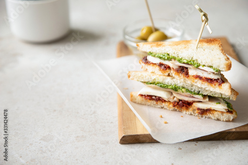 Sandwich with chicken breast, dried tomatoes, mozzarella and pesto with olives on background.