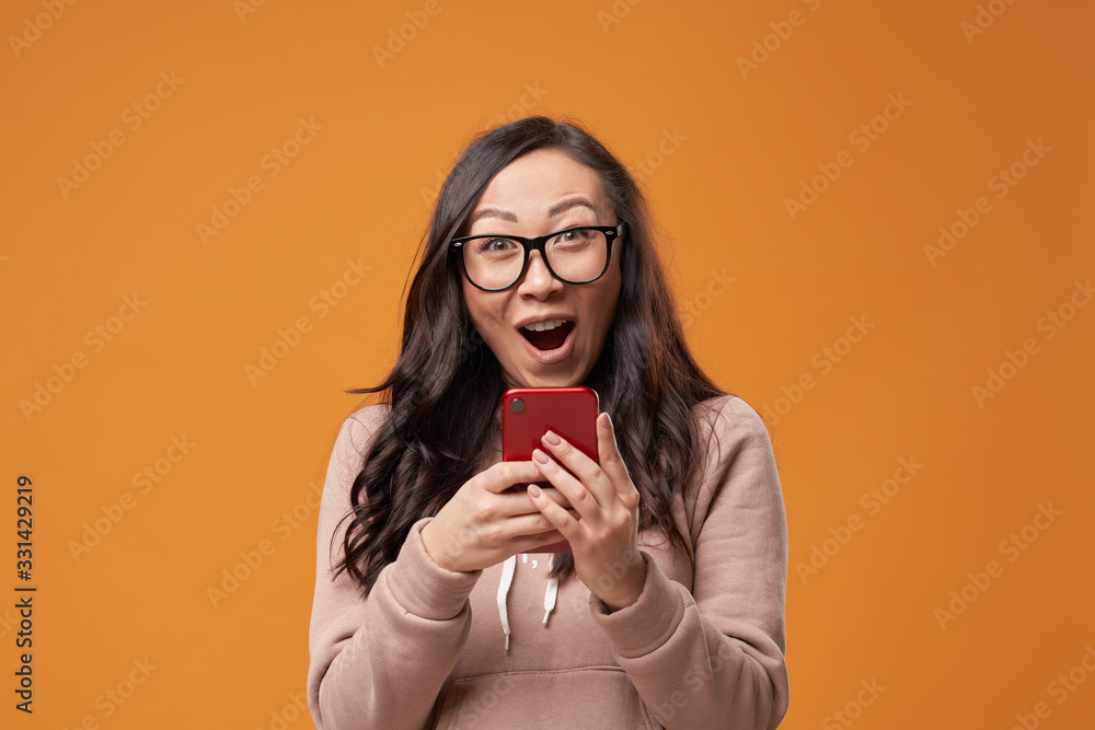 Asian brunette woman in glasses with long hair with phone in her hands isolated in studio Asian brunette woman in glasses with long hair with phone in her hands isolated in studio