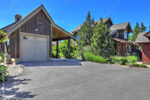 Grey wooden rustic house with white garage door and pine trees and large driveway