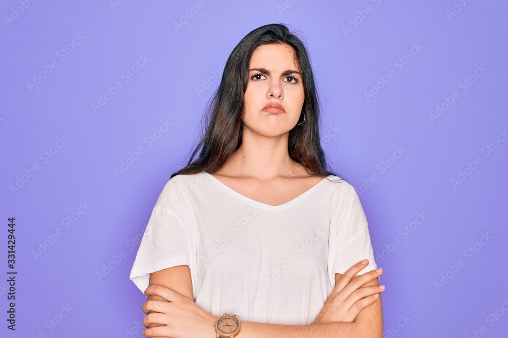 Obraz premium Young beautiful brunette woman wearing casual white t-shirt over purple background skeptic and nervous, disapproving expression on face with crossed arms. Negative person.